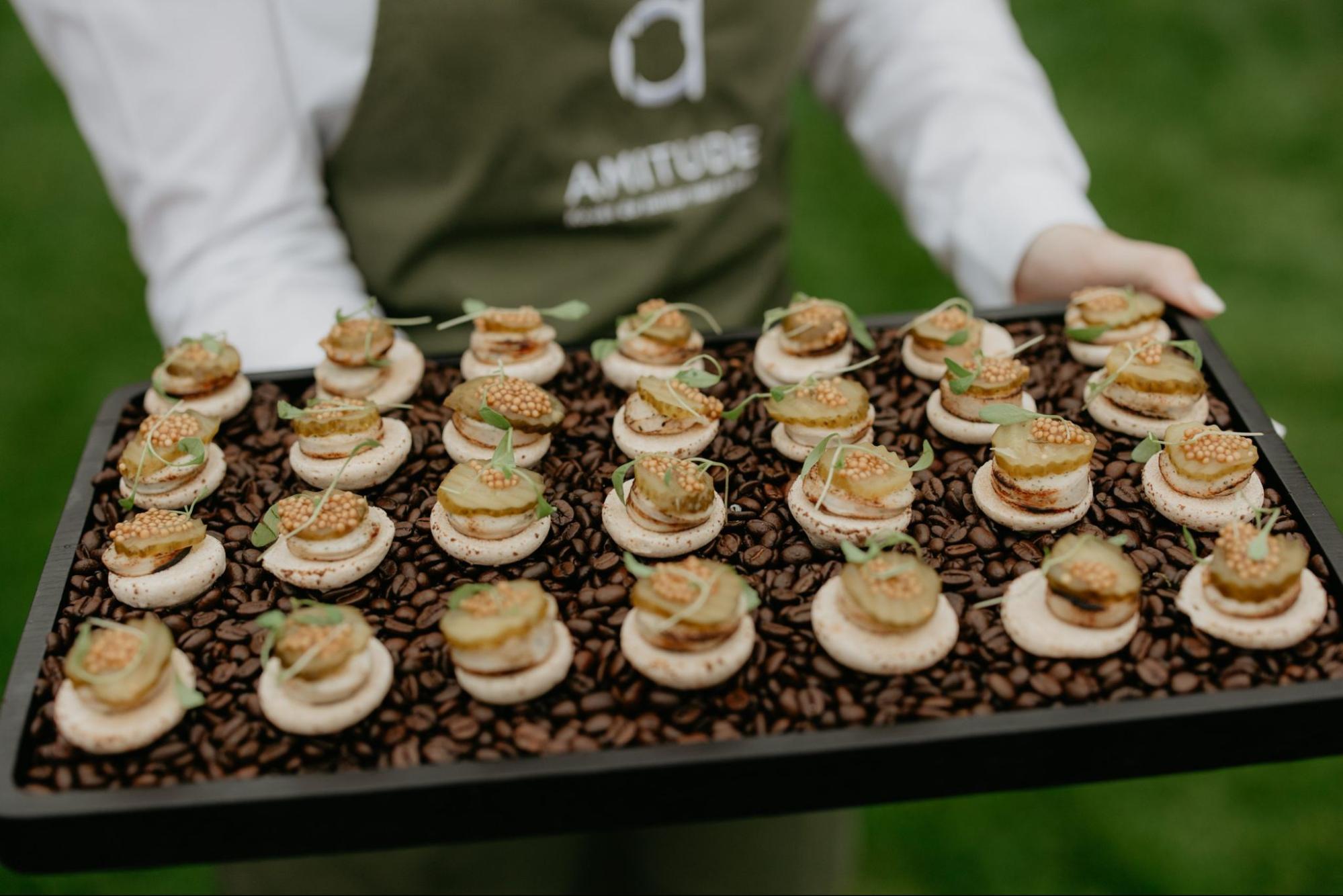 Medewerker in Amitude-schort presenteert verfijnde hapjes op een dienblad