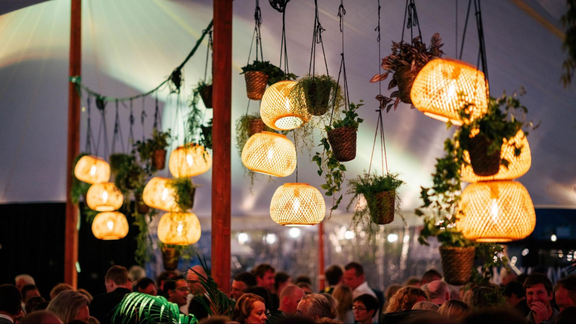 Sfeervolle receptie onder een feesttent met hanglampen en groen bij een avondevent