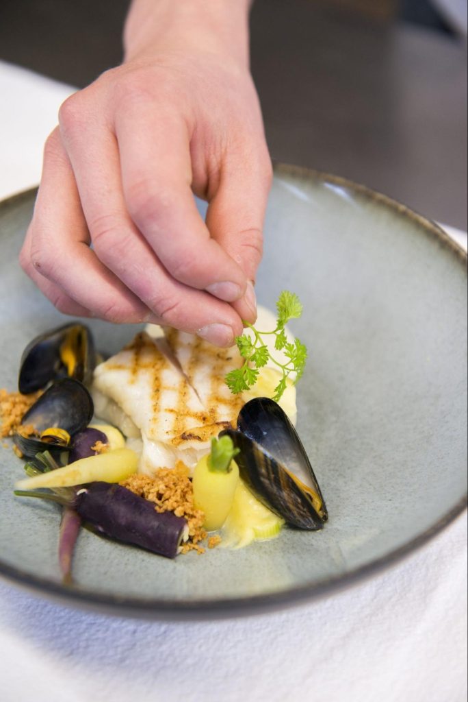 Chef werkt een bord met gegrilde vis, mosselen en groenten af